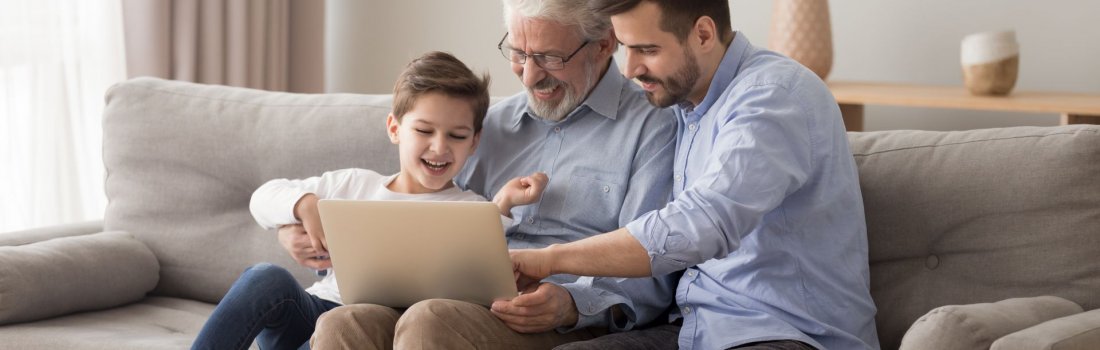 A grandfather using a laptop with his adult son and grandchild